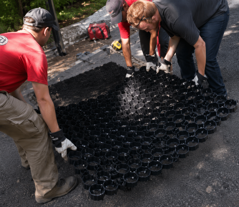 Workers installing black TrueGrid pavers on a paved surface.