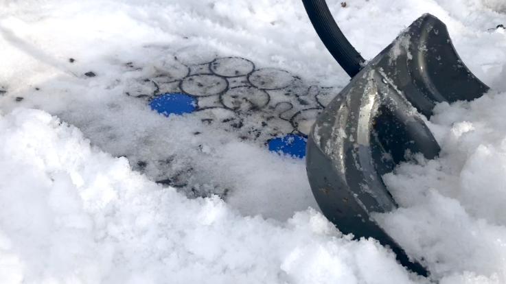Shoveling snow on a gravel driveway with permeable paver system and blue parking markers.
