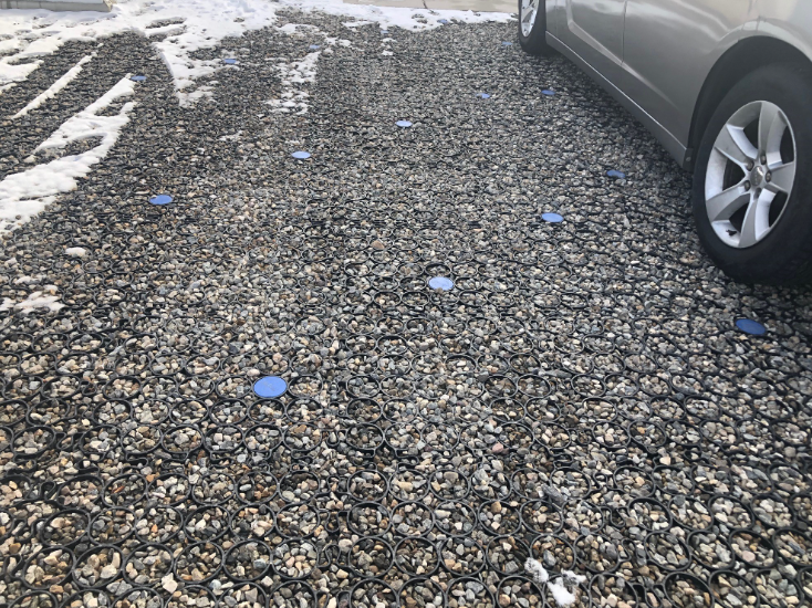 Partially snow covered parking lot with permeable gravel grid and blue markers