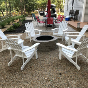 A backyard fire pit with chairs on a gravel yard.