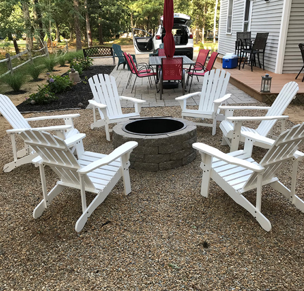 A backyard fire pit with chairs on a gravel yard.