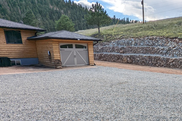 An image of a gravel driveway outside of a small house. 