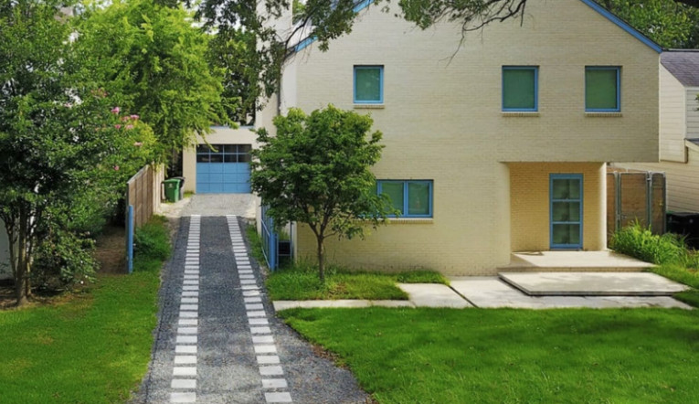 A home showcases concrete wheel paths set in gravel, framed by surrounding greenery.