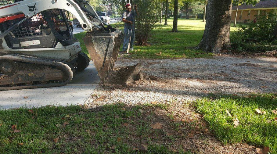 Skid steer removing gravel from a driveway near a lawn.