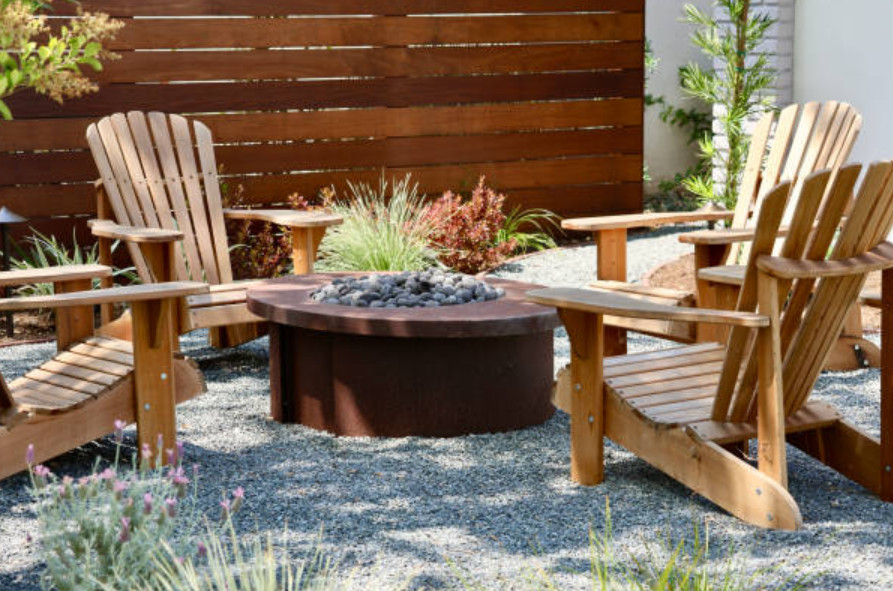 Gravel patio with wooden chairs arranged around a round fire pit.