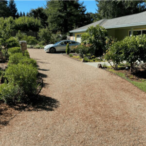 Gravel driveway leading to a house with a parked white car, surrounded by garden landscaping.