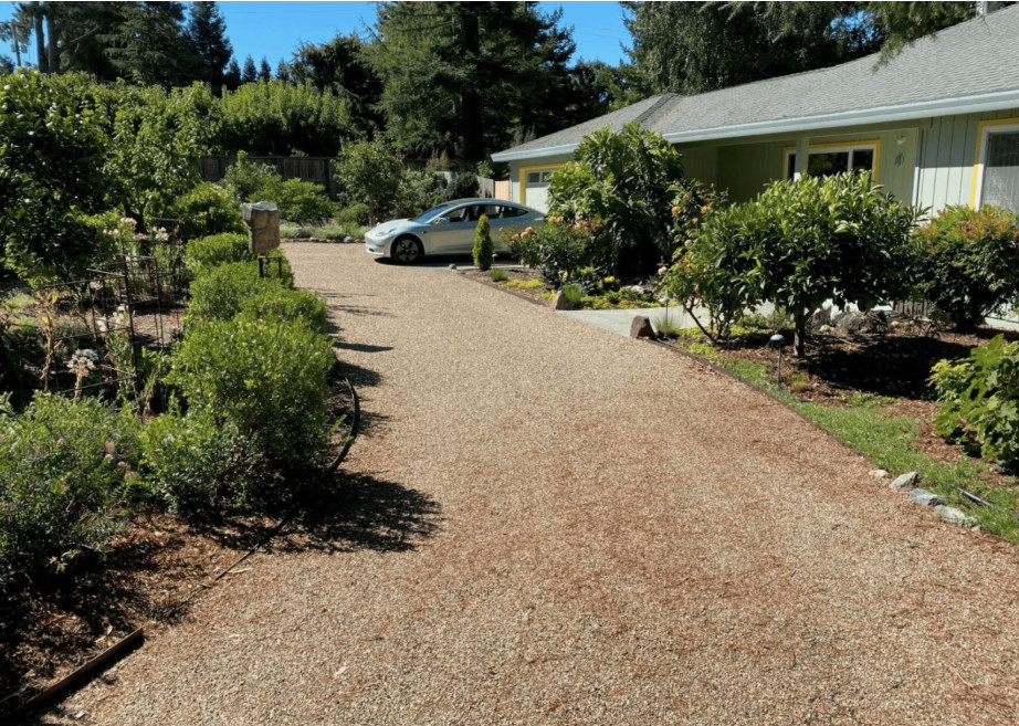 Gravel driveway leading to a house with a parked white car, surrounded by garden landscaping.