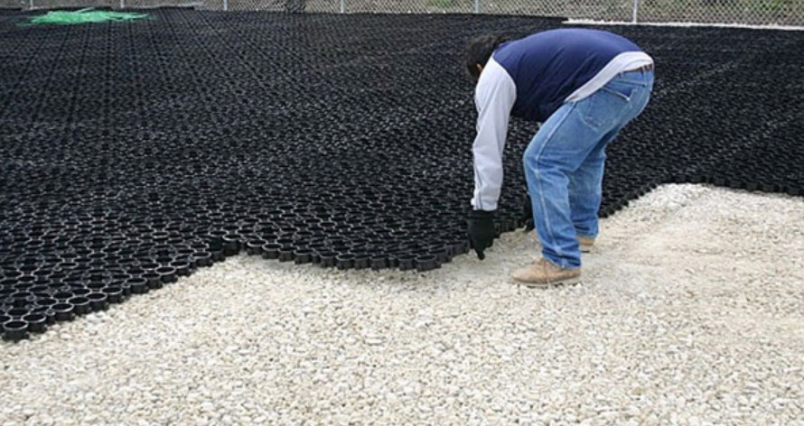 Gravel stabilizer grid partially being placed on drainage rock base layer.