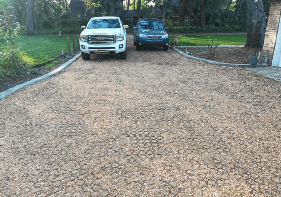 Gravel driveway reinforced with a stabilizer grid, with two parked cars near a house.