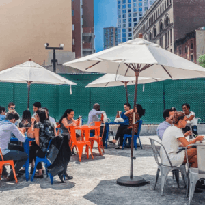 People dining outdoors at café tables with umbrellas in a city setting.