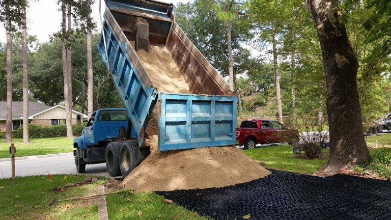 Dump truck unloading sand over permeable plastic pavers during driveway installation.