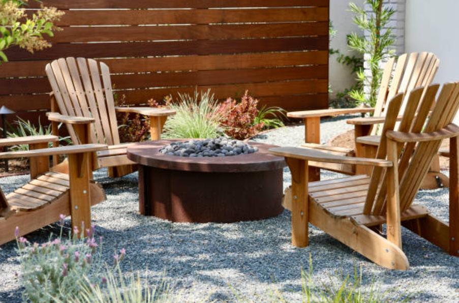 Gravel patio with wooden chairs arranged around a round fire pit.