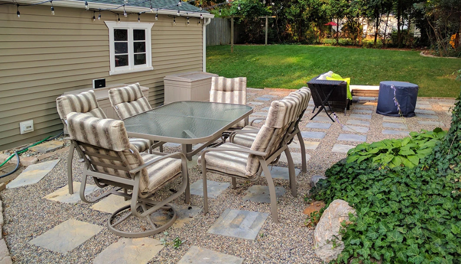 Outdoor patio with gravel flooring, paver stones, and a dining table set beside a garden.