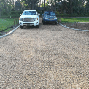 Gravel grid driveway leading to a home with two cars parked at the top.