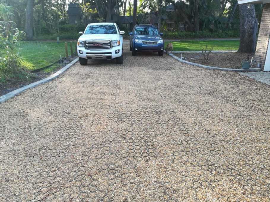 Gravel grid driveway leading to a home with two cars parked at the top.