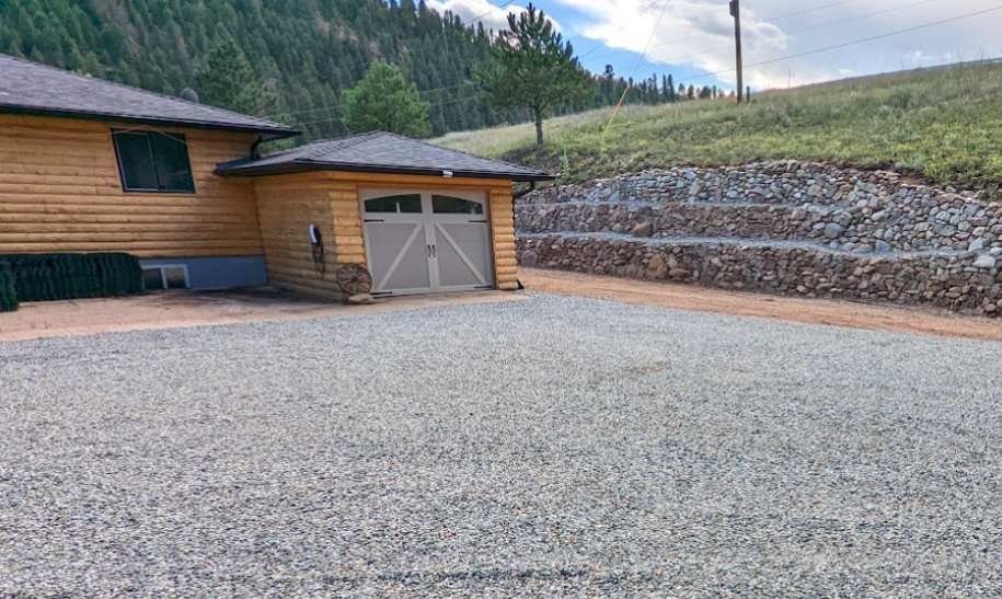 Gravel driveway beside a log cabin home with terraced stone retaining walls.