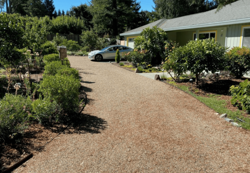 Curved residential driveway featuring gravel between pavers bordered by landscaped garden beds.