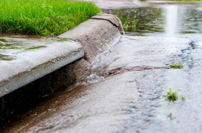 Rainwater flowing along a curb and gutter system as part of home stormwater management.