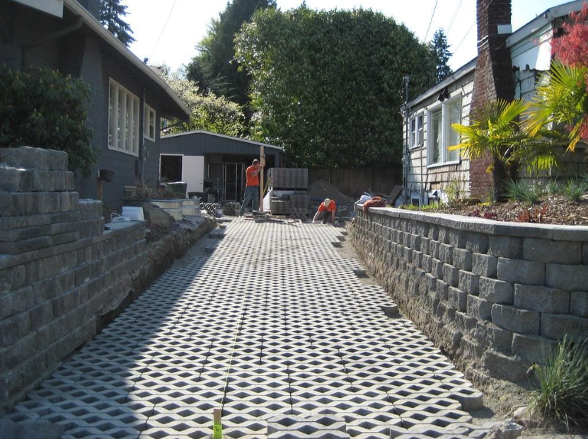 Workers installing permeable paver grids between retaining walls to demonstrate the benefits of permeable pavement in managing runoff.