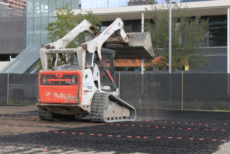 Skid steer installing permeable pavers for a commercial parking lot project.