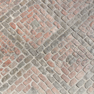 Brick driveway with a herringbone pattern made from weathered red and gray bricks.