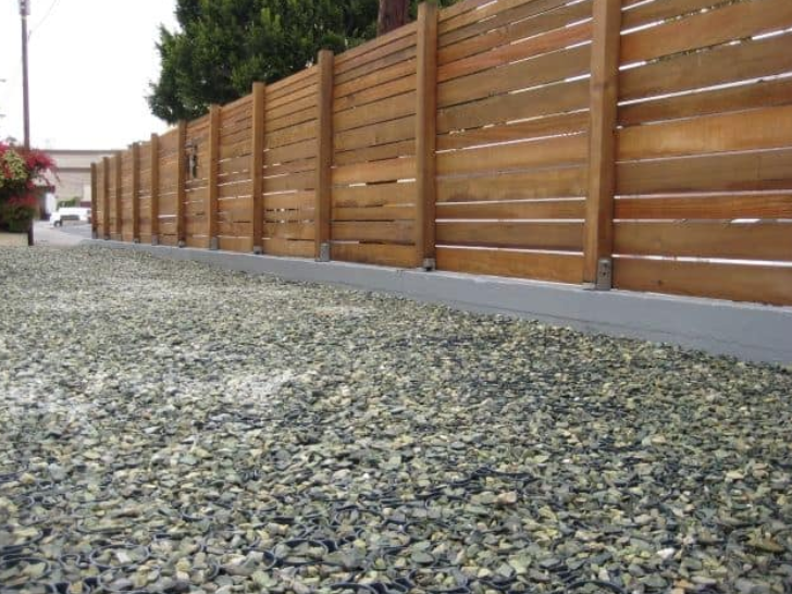 Gravel driveway with permeable pavers installed along a wooden privacy fence for drainage and ground stability.