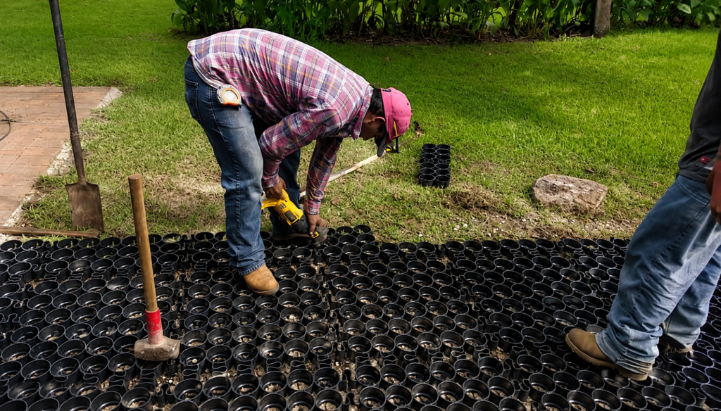 Workers installing a permeable paver grid system in a landscaped area.