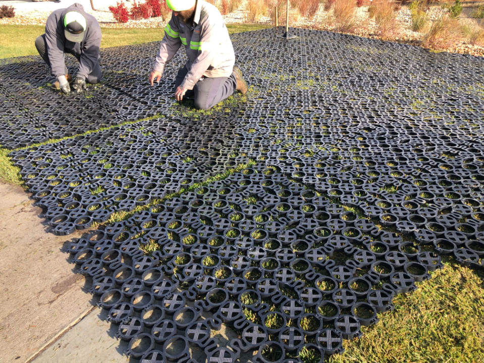 Workers installs ground reinforcement grids to protect a grass surface. 